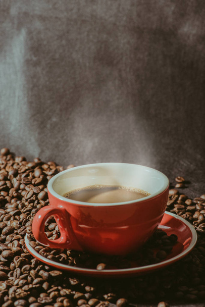 Ζεστό καφέ στο φλιτζάνι κόκκινο και κόκκους καφέ αποτελούν το υπόβαθρο. - Φωτογραφία, εικόνα