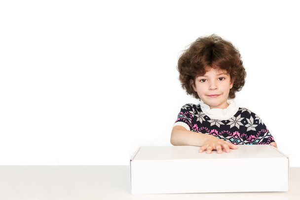 Surprised cute boy holds his hand on the white box, smiling and looking at the camera. White background. - Fotografie, Obrázek