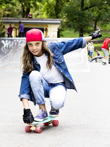 Nettes Mädchen mit Baseballmütze und Skateboard in einem Skatepark. Freizeit. - Foto, Bild