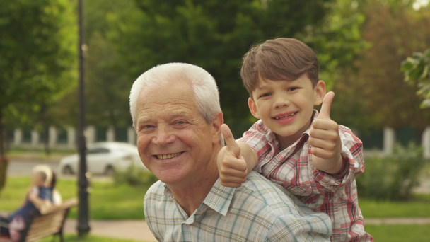Kisfiú a hüvelykujját mutatja fel a grandpas hátán - Felvétel, videó
