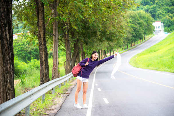 Happy pretty young woman with hand up calling passing car on countryside street, - Foto, Imagen