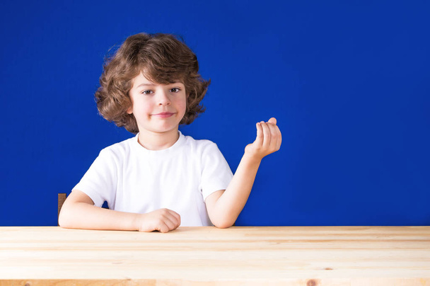 Happy curly cute boy looking at the camera with folded hands "boat". Close-up. Blue background. - Foto, Imagem