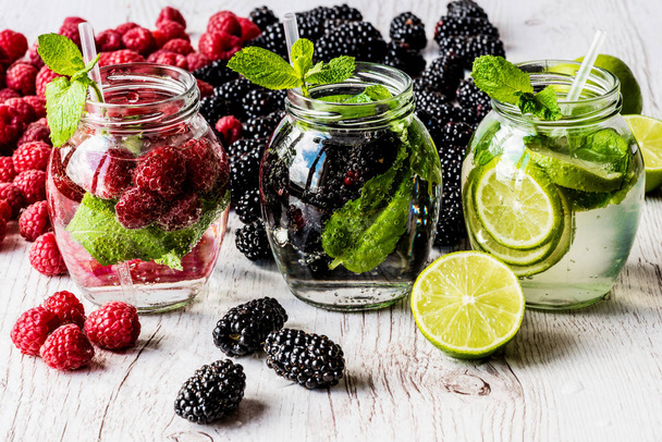 Three kinds of detox water with blackberry, strawberry, lime with ingredients on white wooden background - Photo, Image