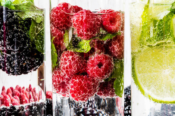 drei Arten von Entgiftungswasser mit Brombeere, Erdbeere, Limette mit Zutaten auf weißem Holzgrund. Supermakro - Foto, Bild