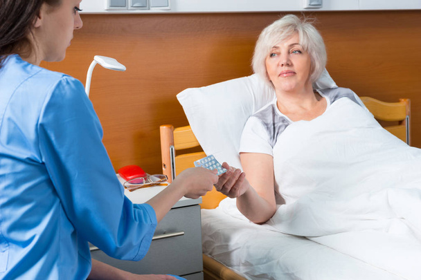 Γυναίκα γιατρό ή νοσοκόμα σε ομοιόμορφο δίνει χάπια για τον ασθενή της - Φωτογραφία, εικόνα