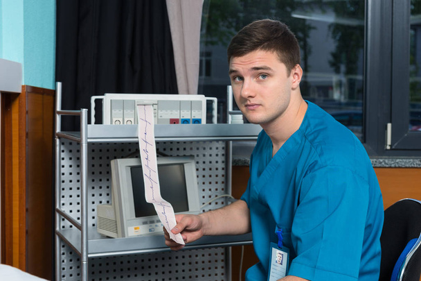 Doctor in uniform is holding analysis of electrocardiograph exam - Foto, afbeelding