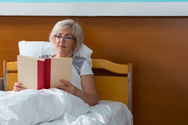 Female patient is reading a book, while lying in the hospital be - Zdjęcie, obraz