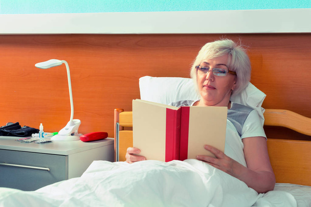 Female patient in glasses is reading a book, while lying in the  - Foto, Imagen