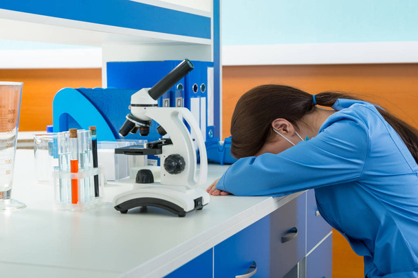 Tired female scientist in uniform is sleaping near her workplace - Fotó, kép