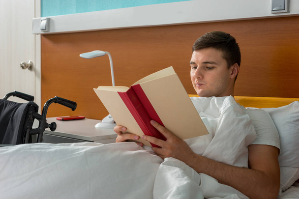 Portrait of male patient lying in the hospital bed and reading a - Foto, afbeelding