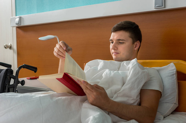 Portrait of young ill patient lying in the hospital bed and read - Fotoğraf, Görsel