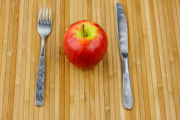 Apfel liegend auf einer Bambusserviette mit Besteck - Foto, Bild
