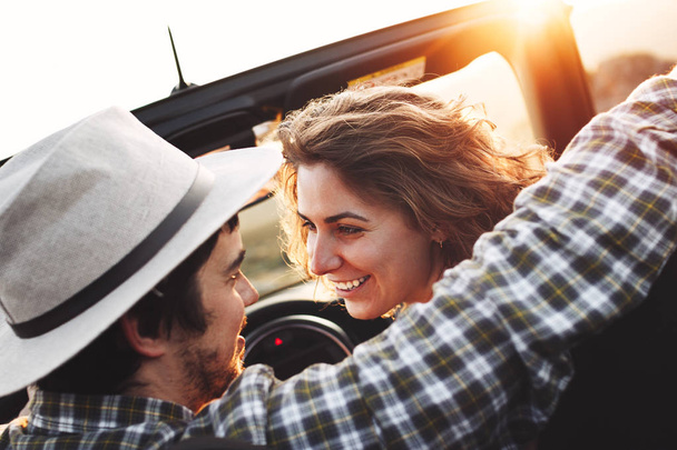 Young loving couple looking at each other sitting in car on background of mountain landscape and sunset. Happy loving couple in a cabriolet - Foto, Bild