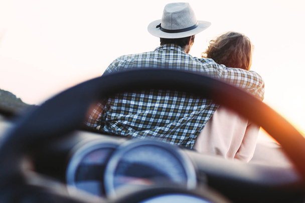 Trendy love couple hipsters sit on hood of cabriolet car and enjoy sunset in mountains - Foto, Bild