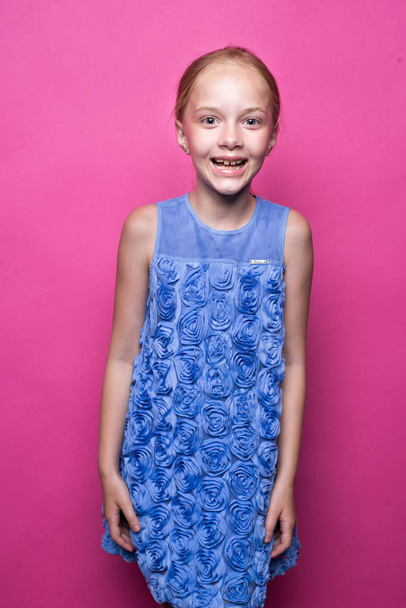 Beautiful little redhead girl in blue dress posing like model on pink background. - Foto, afbeelding
