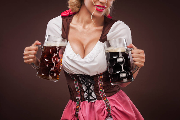 Closeup portrait of boyd Oktoberfest girl - waitress, wearing a traditional Bavarian dress, serving big beer mugs on black background. - Φωτογραφία, εικόνα
