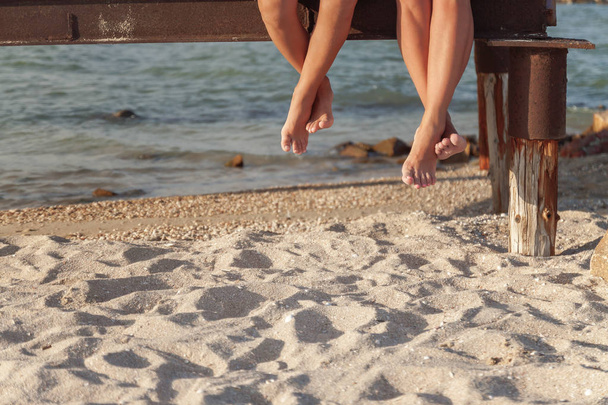 due paia di gambe penzolanti sulla sabbia della spiaggia
 - Foto, immagini