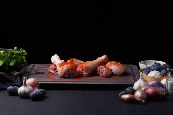 Κινηματογράφηση σε πρώτο πλάνο από νωπό κοτόπουλο με σκόρδο, πάπρικα, αλάτι και πιπέρι μείγμα σε σκούρο φόντο. Γύρω από την κοπή του σκάφους επίσης κρεμμύδια και δαμάσκηνα. Χώρο αντίγραφο - Φωτογραφία, εικόνα