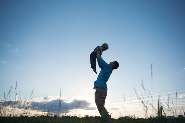 silhouette of father holding his son above in the park - Foto, afbeelding