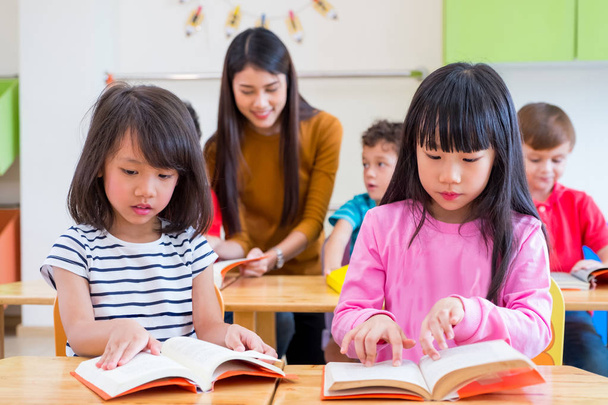 two Asian girl kid reading book in classroom and while teacher t - Fotó, kép