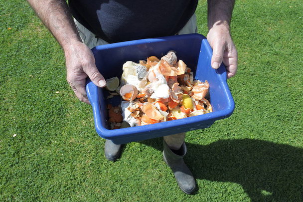 Πρωτου προσωπου (άποψη) της ώριμος άνδρας φέρει ένα δοχείο γεμάτο εγχώριων τροφίμων αποβλήτων, έτοιμο να λιπαθεί στον εγχώριο κήπο. Περιβάλλοντος και ανακύκλωσης έννοια των τροφίμων. χώρο αντίγραφο - Φωτογραφία, εικόνα