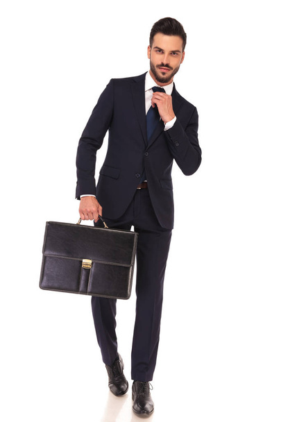 business man holding briefcase is fixing his tie and walks - 写真・画像