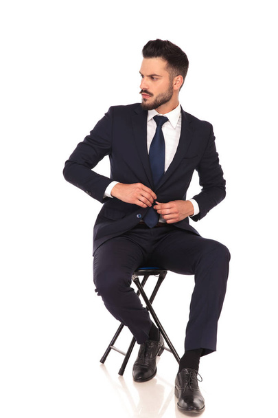jonge zakenman zittend op een stoel en knopen zijn pak. - Foto, afbeelding