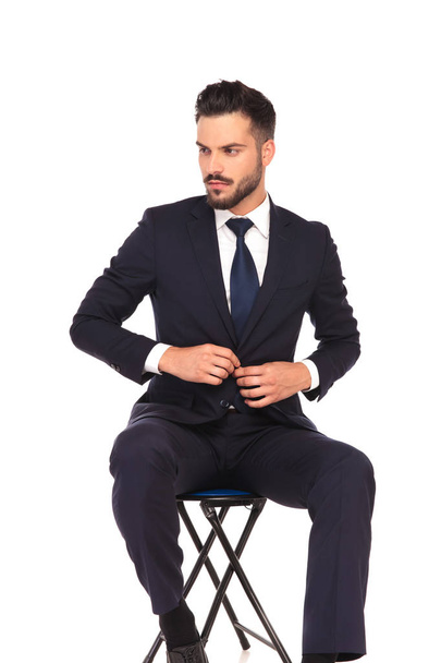 Geschäftsmann schließt seinen Anzug und blickt im Sitzen zur Seite  - Foto, Bild