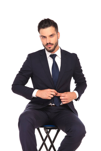 joven hombre de negocios sentado en la silla y abotonando su abrigo
  - Foto, imagen