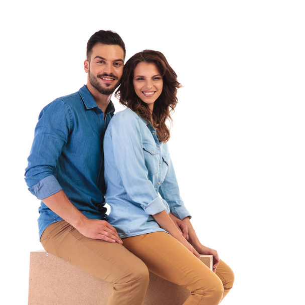 smiling casual couple sitting together on wooden box  - Φωτογραφία, εικόνα
