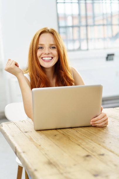 Young smiling red-haired woman using laptop - Fotó, kép