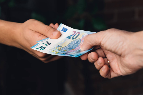 Рука жінки дає молодому чоловікові євро гроші
 - Фото, зображення