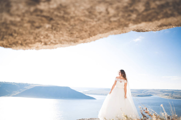 Pretty lady, bride posing in a wedding dress near sea on sunset - Фото, изображение