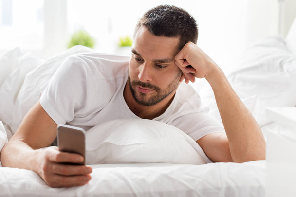young man with smartphone in bed in morning - Fotoğraf, Görsel
