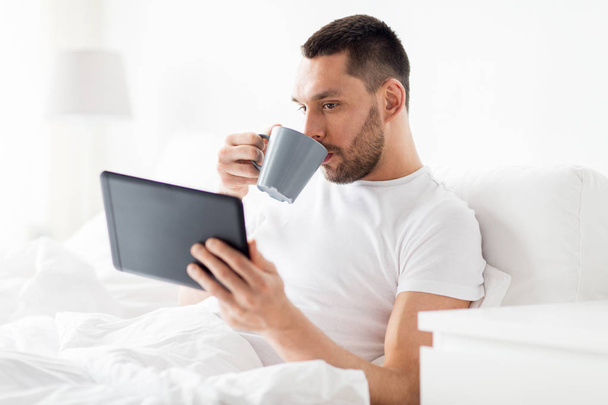 man with tablet pc drinking coffee in bed at home - Fotó, kép