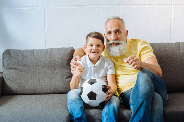 Upbeat grandfather and grandson supporting their favorite football team - Foto, Imagen