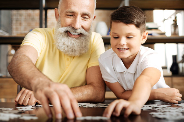 Upbeat grandfather and grandson solving jigsaw puzzle - Foto, afbeelding