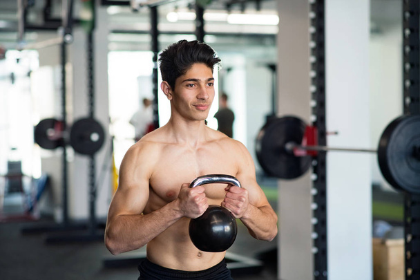 Young fit hispanic man in gym exercising with kettlebell. - Foto, afbeelding