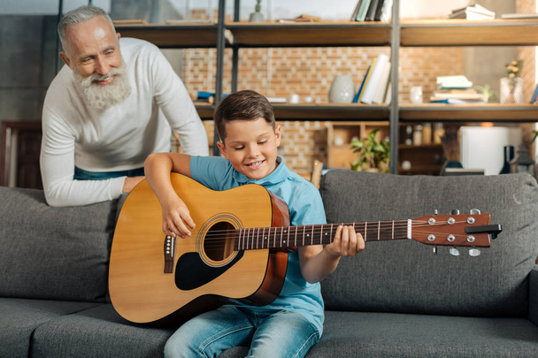 Grandfather watching his grandson play guitar - Photo, image