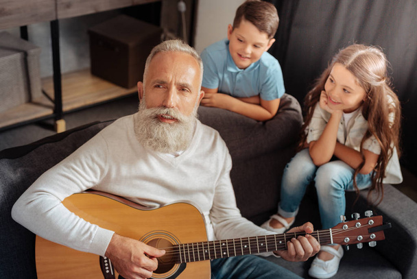 Inspired senior man playing guitar for his grandchildren - Foto, afbeelding
