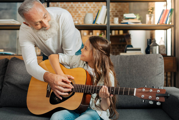 Loving grandfather teaching his granddaughter how to play guitar - Valokuva, kuva
