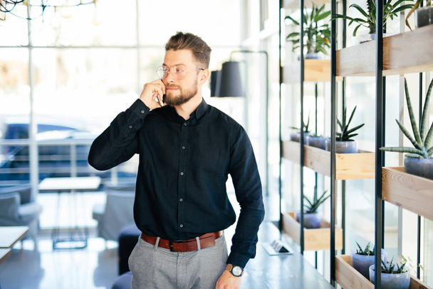 Young bearded business man in office talking at mobile phone in modern office - Photo, Image