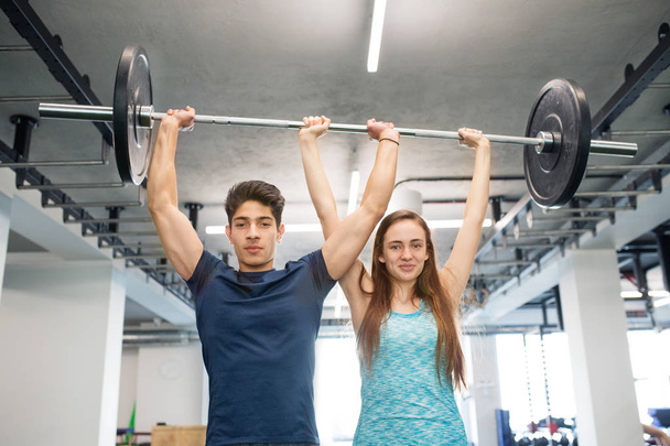 Young fit couple in gym lifting heavy barbell. - Φωτογραφία, εικόνα
