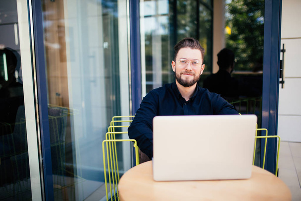 Homem de negócios barbudo sorridente no telefone trabalhando em laptop fora do café
 - Foto, Imagem