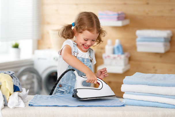 Menina feliz engomar roupas na lavanderia
   - Foto, Imagem
