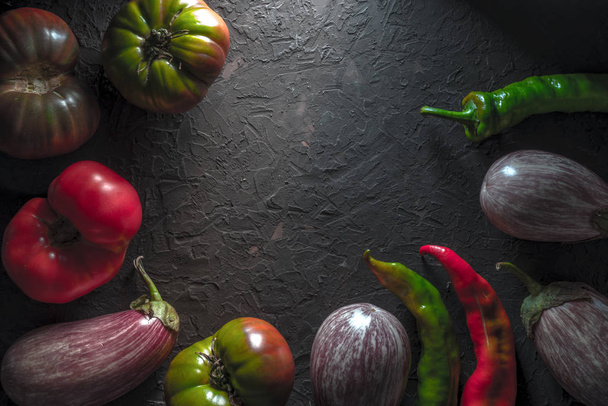 Frame of multi-colored tomatoes, aubergine and chili on a gray table free space - Foto, Imagem