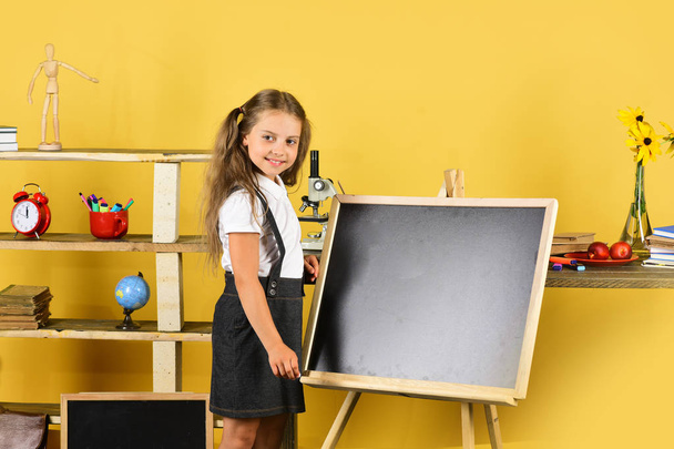 Schoolgirl with smiling face near bookshelf with school items - Zdjęcie, obraz