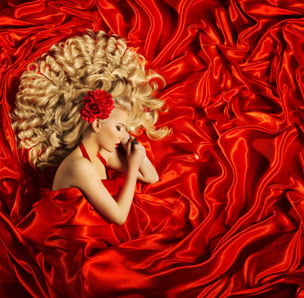 Haar schoonheid kunst, vrouw mooi krullend kapsel, blond fotomodel slapen op rode zijde stof - Foto, afbeelding