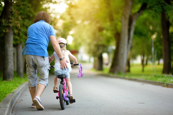 father teaching daughter to ride bicycle - 写真・画像