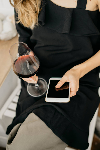 Vrouw met wijn in de hand houden van de telefoon - Foto, afbeelding